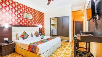 Quarto de hotel com cama, guarda-roupa, escrivaninha e televisão.