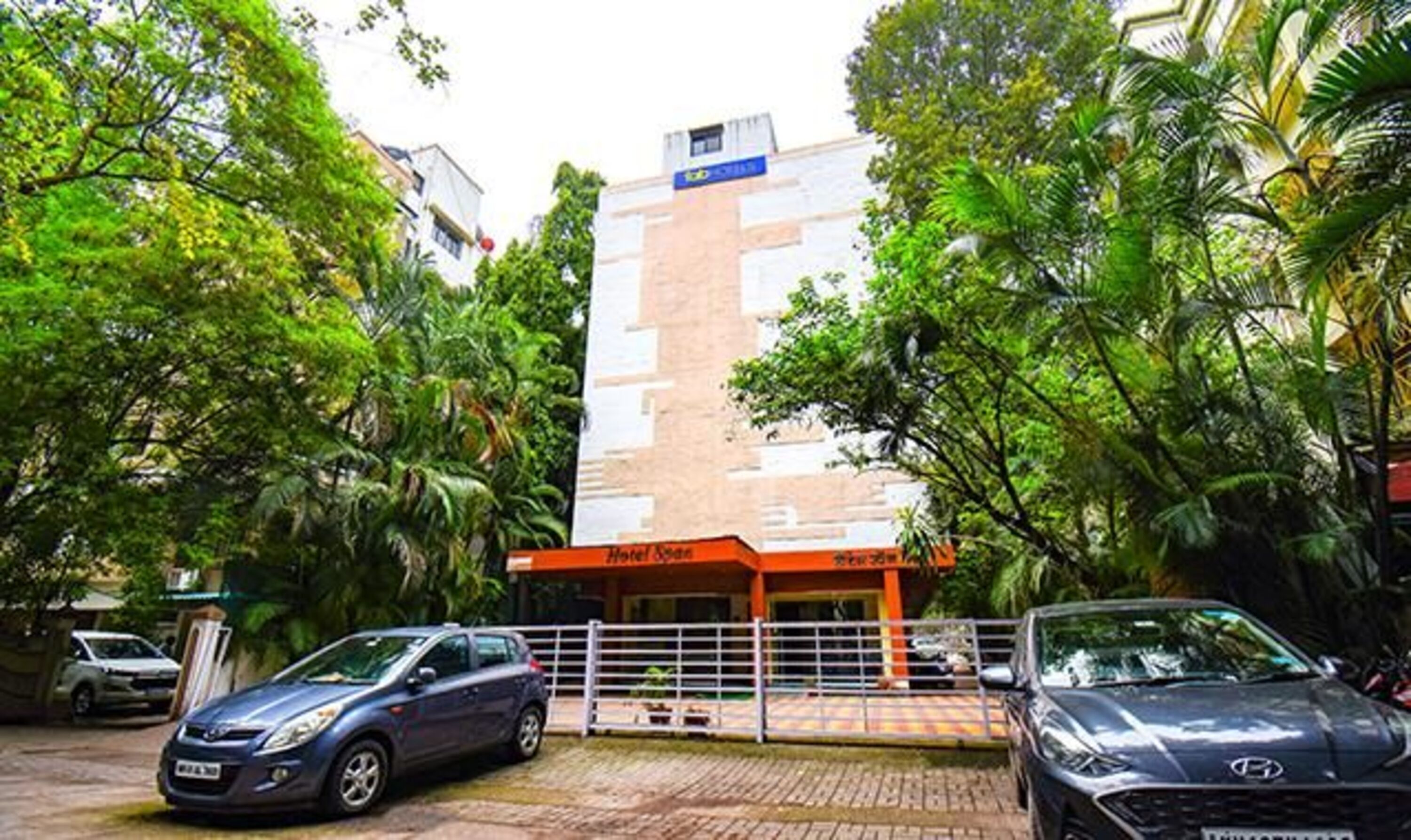 A hotel entrance with a modern building, a gated driveway, and parked cars.
