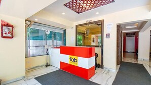 A hotel reception area with a red and white counter, a window with a view, and a door leading to another room. - Fabhotel Envirosafe Stays (Pune)