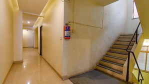 A hallway with a fire extinguisher mounted on the wall, a staircase with metal railings, and a door at the end of the hallway. - Fabhotel Rs Apartment (Pune)