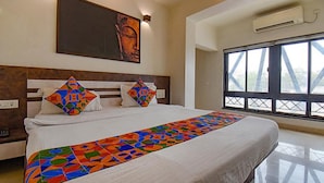 A modern hotel room with a large bed, a colorful geometric bed runner, a large window with a view of a bridge, and an air conditioning unit on the wall. - Fabhotel Rs Apartment (Pune)