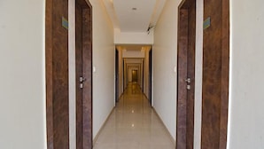 A long, narrow hallway with wooden doors on either side and a tiled floor. - Fabhotel Rs Apartment (Pune)