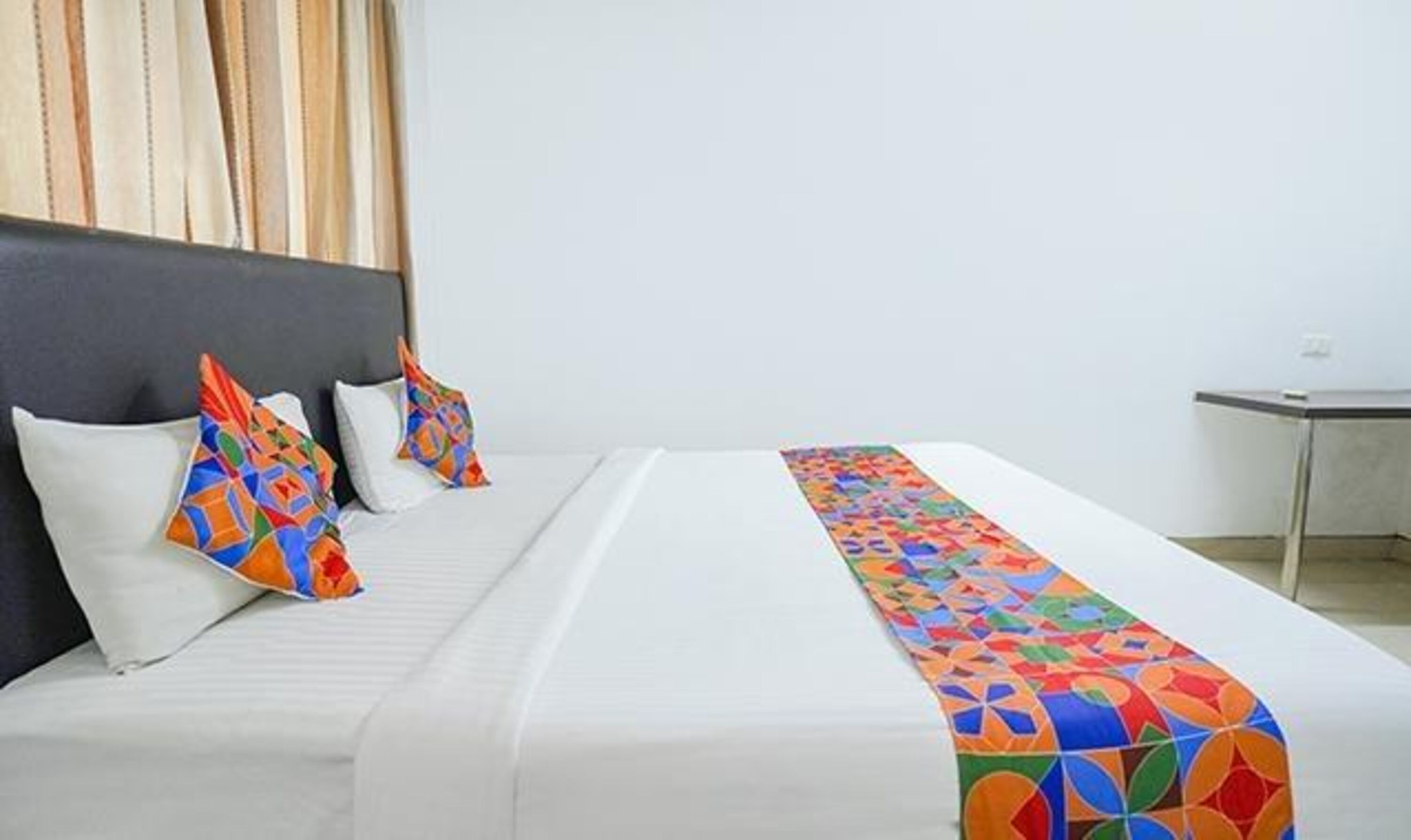 Una habitación de hotel con una cama, almohadas y una manta colorida.