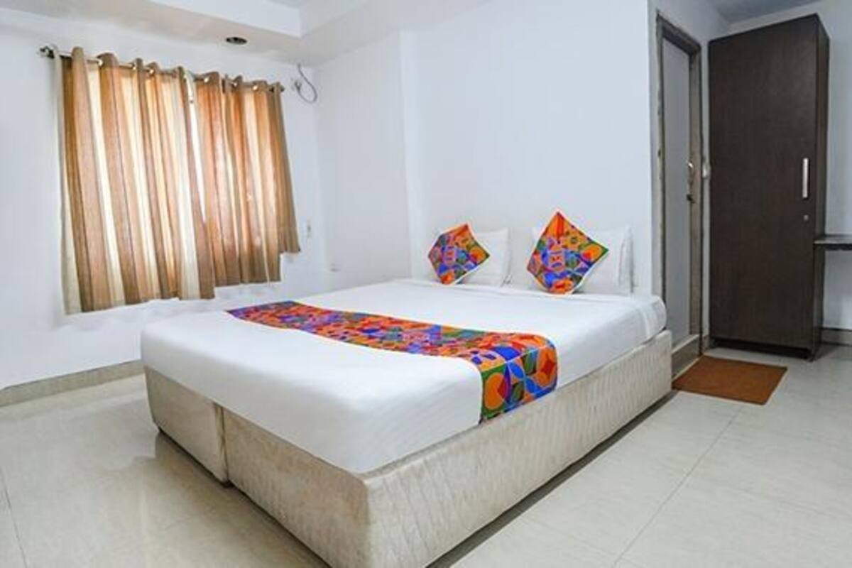 A hotel room with a large bed, a window with curtains, a door, and a tiled floor.