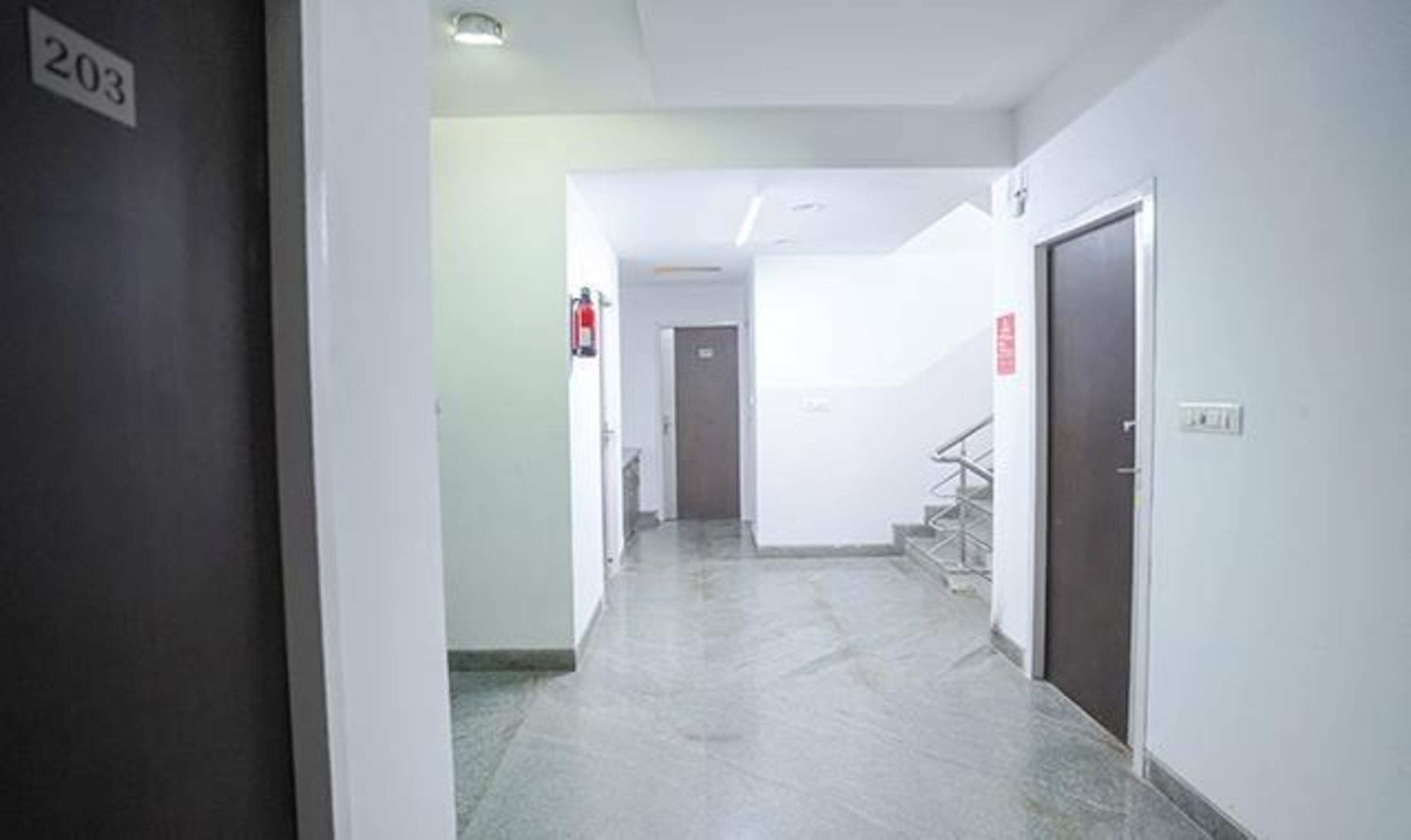 A hallway with a marble floor, a fire extinguisher, and a door marked with the number 203.