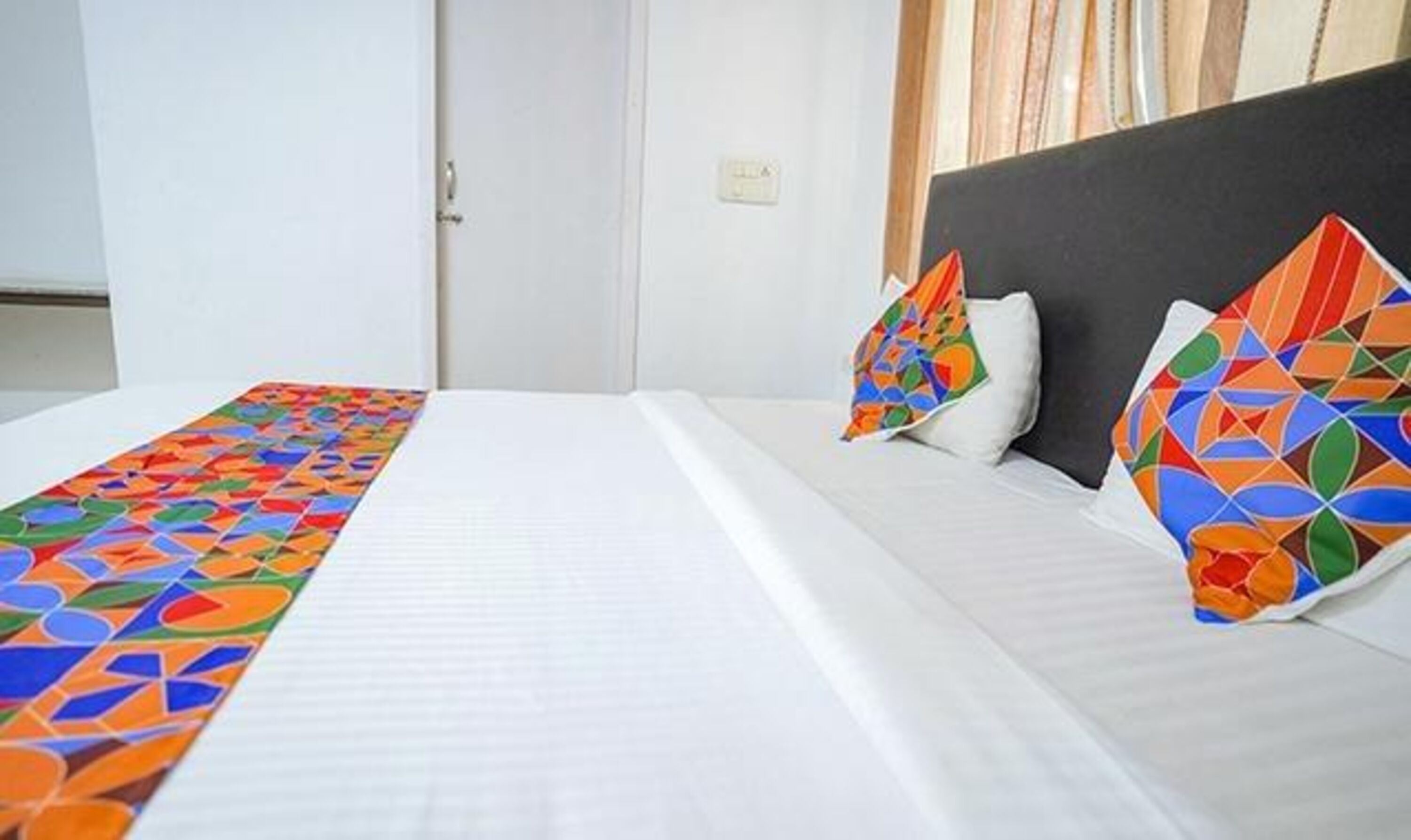 A hotel room with a neatly made bed, a headboard, and a window with curtains.