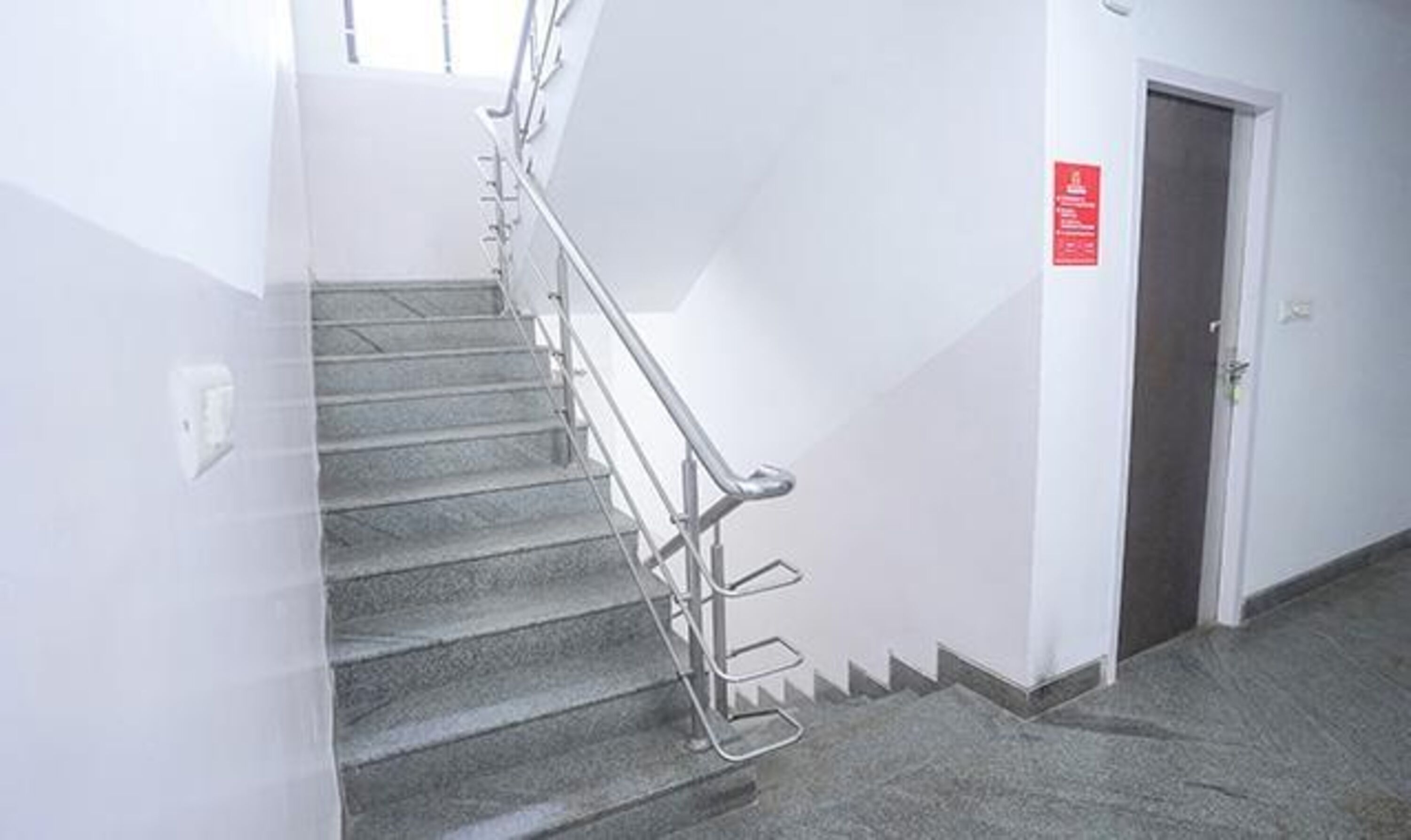 A staircase with metal handrails, a door with a red sign, and a carpeted floor.