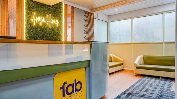 A hotel reception area with a neon sign reading "Royal Homes" and a sign for "fab hotels" on the counter. There are two sofas and a patterned rug on the floor. - Fabhotel Aursai (Pune)