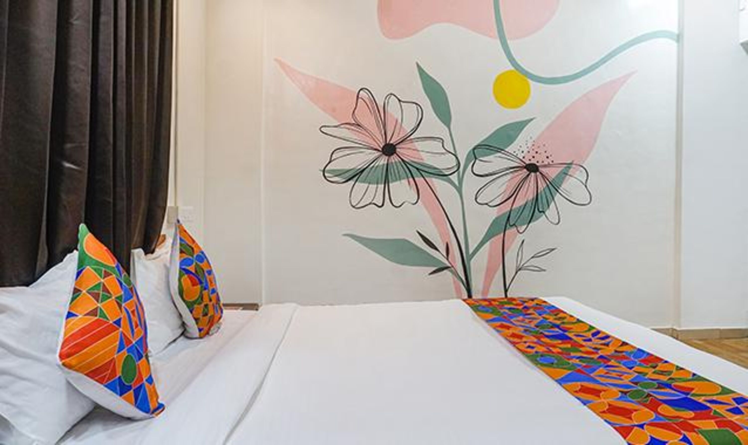 A hotel room with a bed, colorful pillows, and a wall mural of flowers.