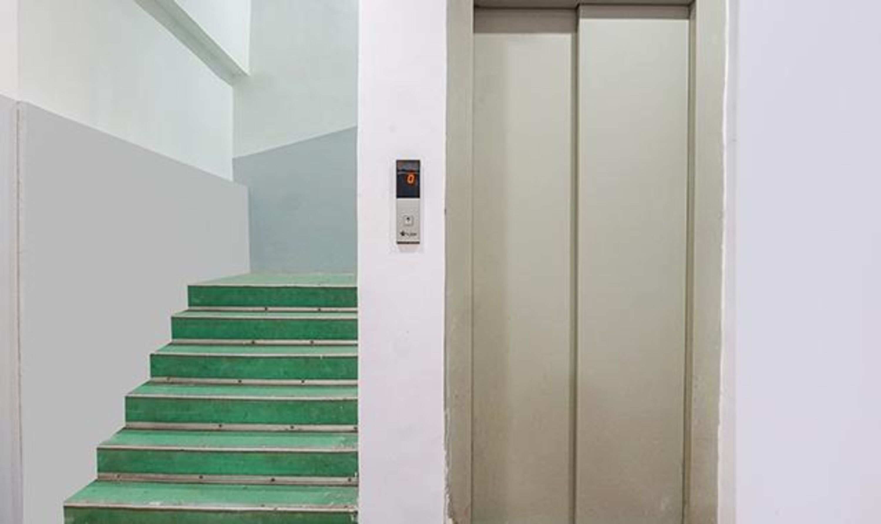 A staircase with green steps leading to a white wall, and an elevator door is visible to the right.