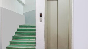 A staircase with green steps leading to a white wall, and an elevator door is visible to the right. - Fabhotel Aursai (Pune)