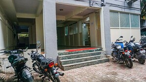 A building entrance with steps leading up to a door, a parking area with motorcycles, and a clear sky. - Fabhotel Aursai (Pune)