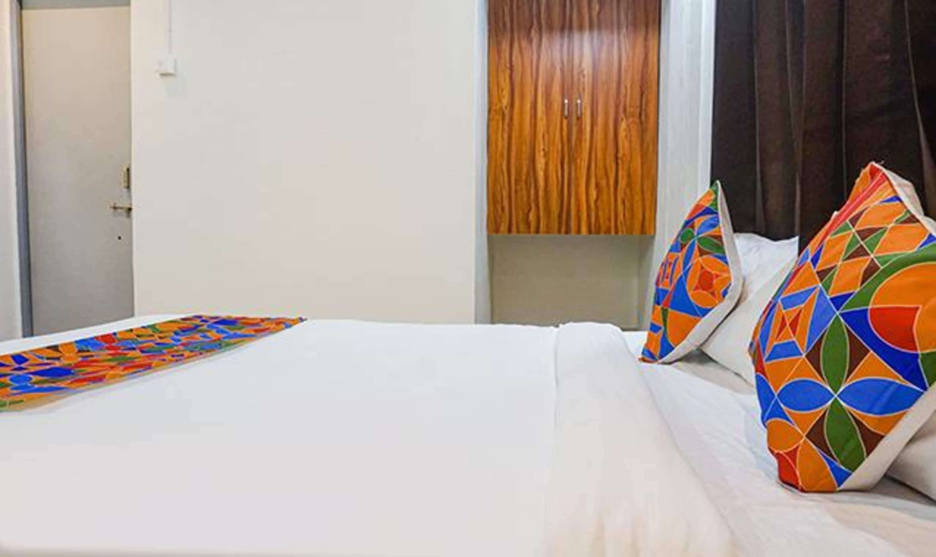A hotel room with a bed, colorful pillows, and a geometric-patterned throw.