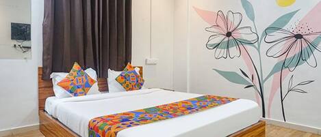 A neatly made bed with a colorful geometric-patterned bedspread, a dark curtain, and a wall with a floral mural.