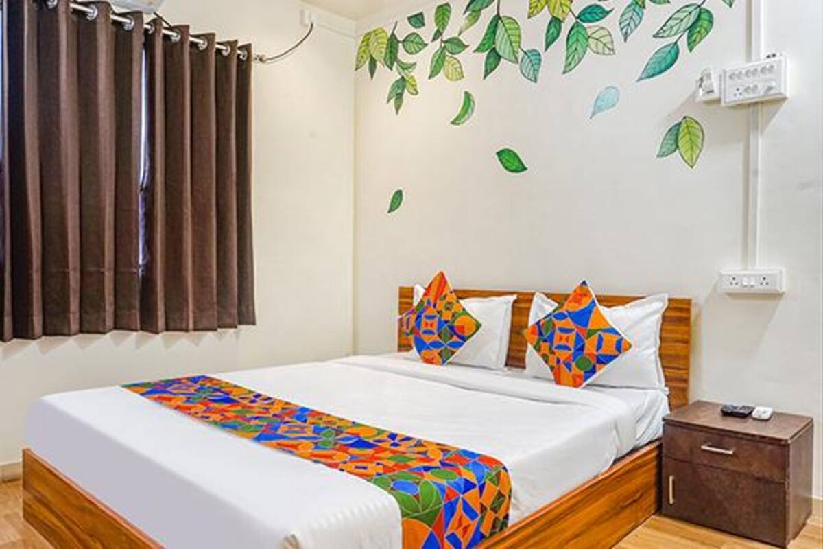 A bedroom with a bed, curtains, a wall with leaf decals, a bedside table, and a nightstand.