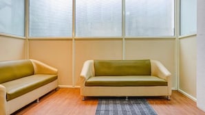 A room with two sofas, a patterned rug, and large windows. - Fabhotel Aursai (Pune)