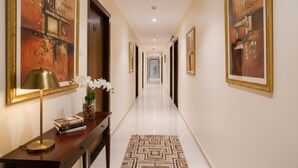 A long, well-lit hallway with framed artwork on the walls, a wooden console table with books and a vase of flowers, and a patterned rug on the floor. - Via Wynd (Mumbai)