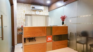 A reception area with a wooden desk, a clock, and a vase with red flowers. - Via Wynd (Mumbai)