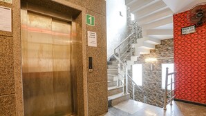 An elevator with a green sign indicating room number 1, a welcome mat, and a staircase with a red textured wall and a fan. - Fabhotel Mng (Kanpur)