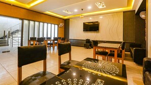 A modern dining area with wooden chairs and tables, a flat-screen TV mounted on the wall, and a staircase leading to an upper level. - Fabhotel Mng (Kanpur)