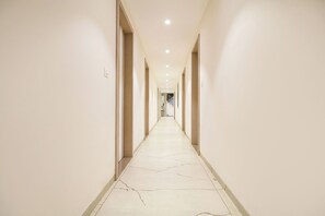 Um corredor comprido e estreito, com paredes claras e piso estampado, que leva a uma escadaria.