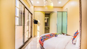 A hotel room with a large bed, a sliding glass door, a small bathroom, and a wardrobe. - Fabhotel Seven Hills (Mumbai)