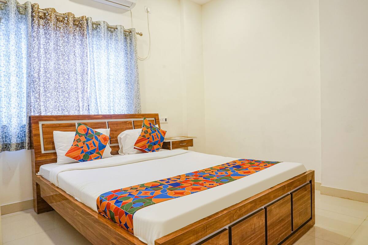 A neatly made bed with a patterned bedspread, a wooden headboard, and two pillows with geometric designs.