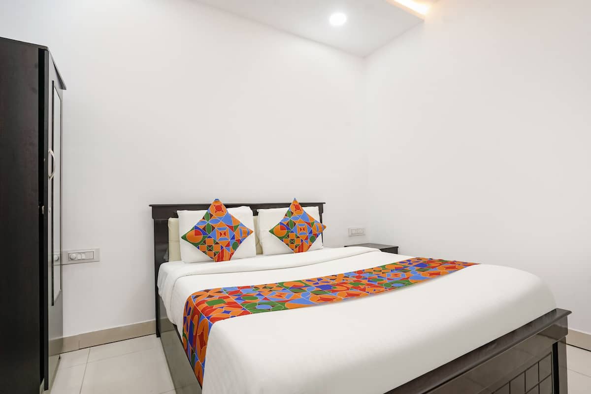 Una cama bien hecha con una colcha de estampado geométrico y colores vivos, un cabecero oscuro y dos almohadones decorativos.
