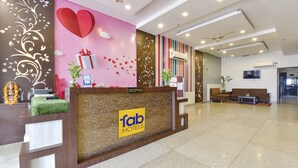 A hotel reception area with a modern design, including a reception desk, a seating area with a sofa and armchairs, and a television mounted on the wall. - Fabhotel The Palm (Jaipur)