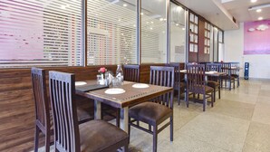 A restaurant with wooden tables and chairs, large windows with blinds, and a wall with a colorful abstract design. - Fabhotel The Palm (Jaipur)