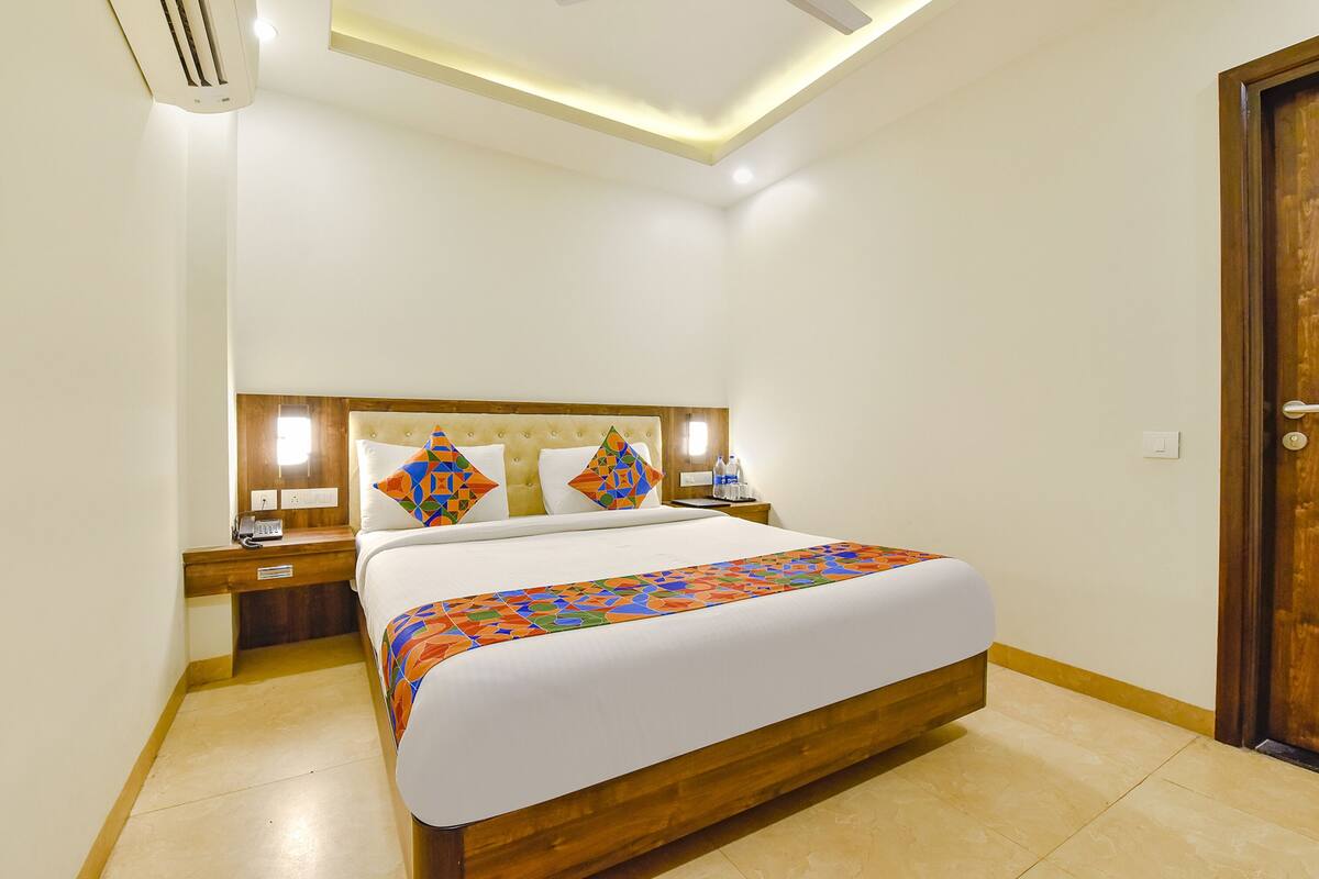 Quarto de hotel com uma cama, mesas de cabeceira, painel de madeira na cabeceira e uma porta.