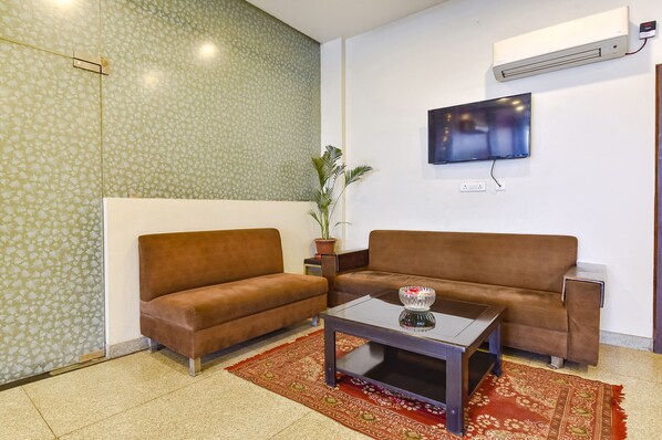 A living room with two brown sofas, a coffee table, a potted plant, and a wall-mounted TV. - Fabhotel The Palm (Jaipur)