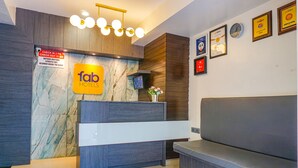 Zona de recepción de hotel con pared de mármol, mostrador de registro y área de descanso.