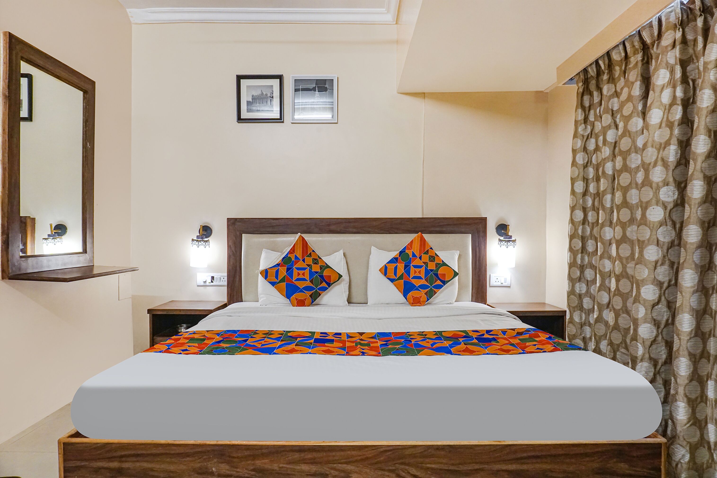 A hotel room with a bed, two bedside tables, a mirror, and a window with curtains.