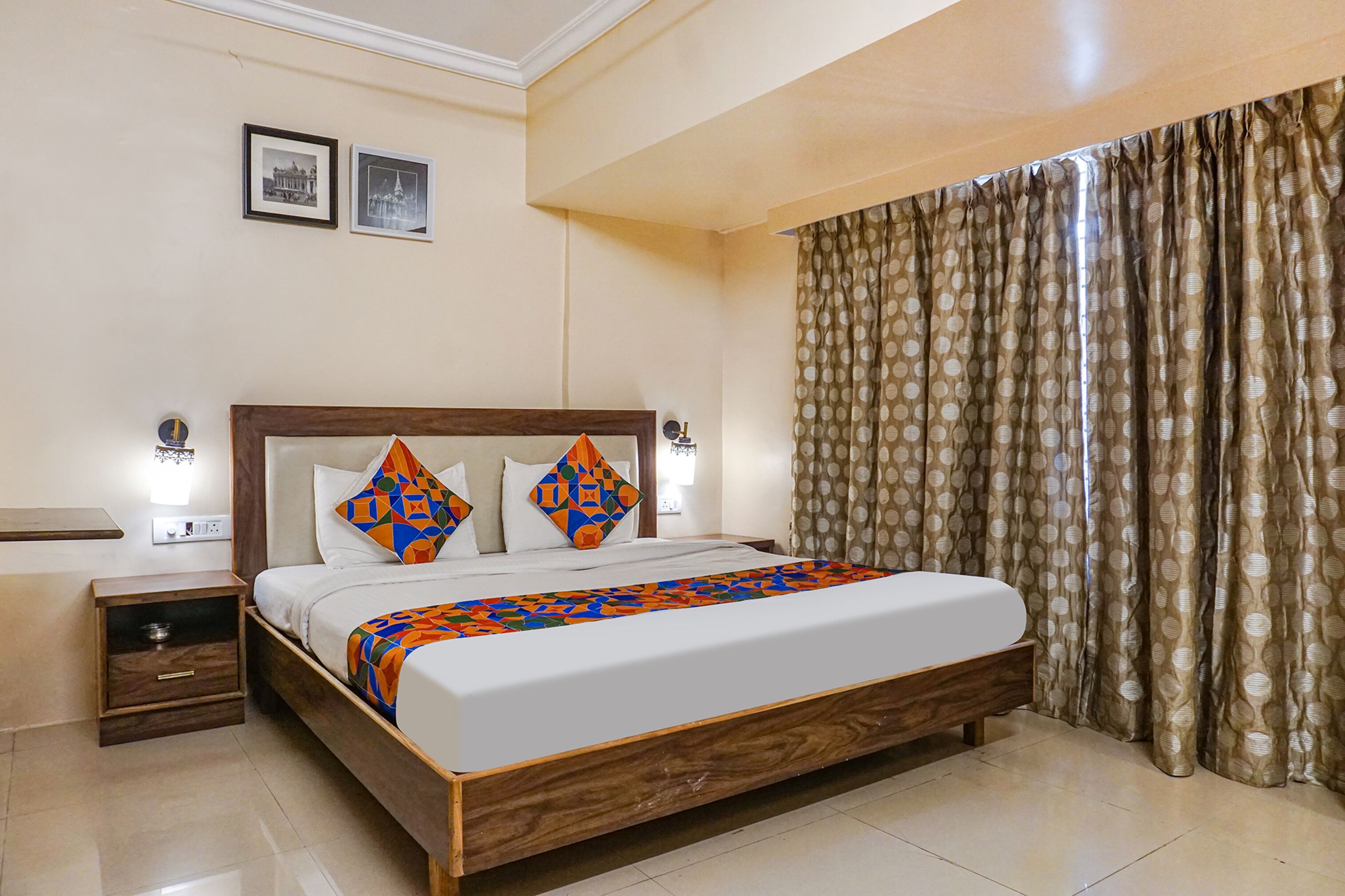 A neatly made bed with a geometric-patterned blanket, two pillows, and a wooden headboard. There is a nightstand with a lamp, and a window with patterned curtains.