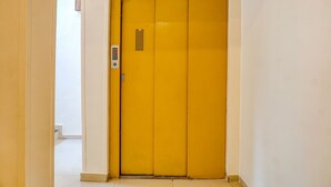 Puerta de ascensor amarilla con panel de control y rejilla de ventilación.