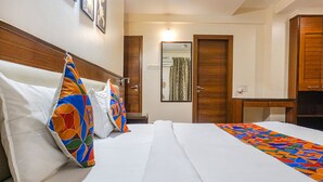 Habitación de hotel con una cama bien hecha, cabecera de madera, un espejo y una puerta con una toalla colgada.