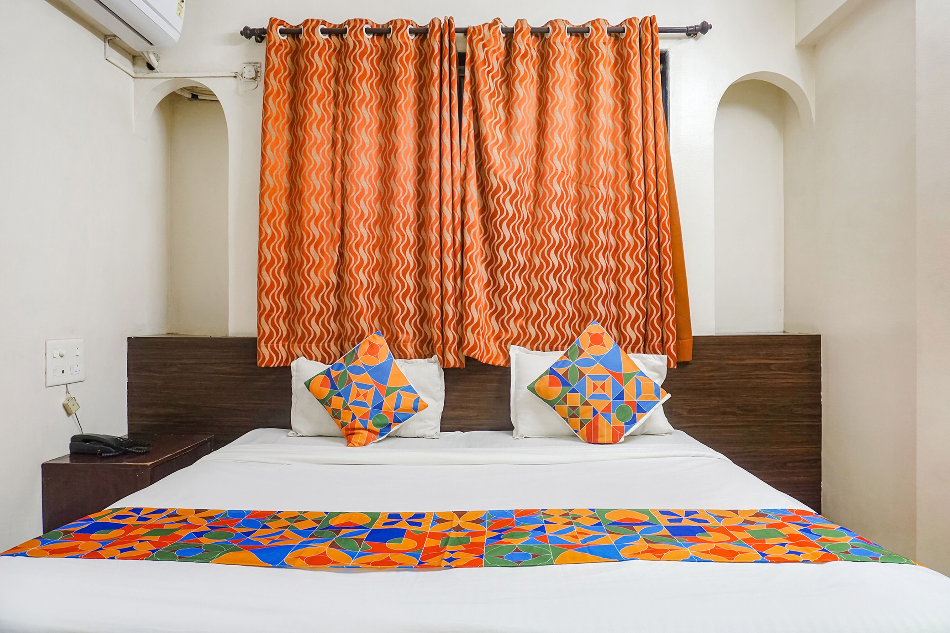 A hotel room with a bed, two pillows, a telephone, and a patterned bedspread.