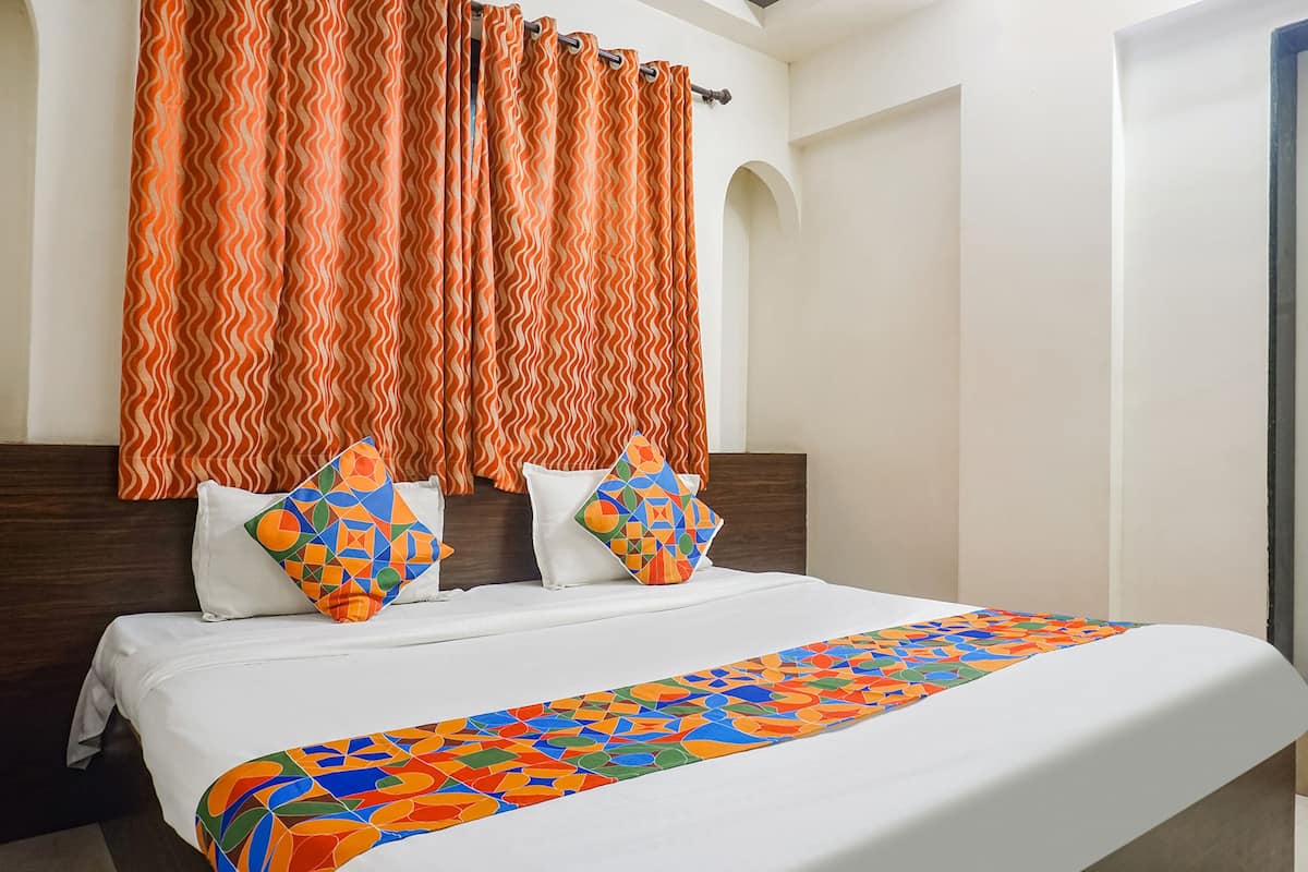 A hotel room with a bed, two pillows, a colorful bedspread, and orange curtains.