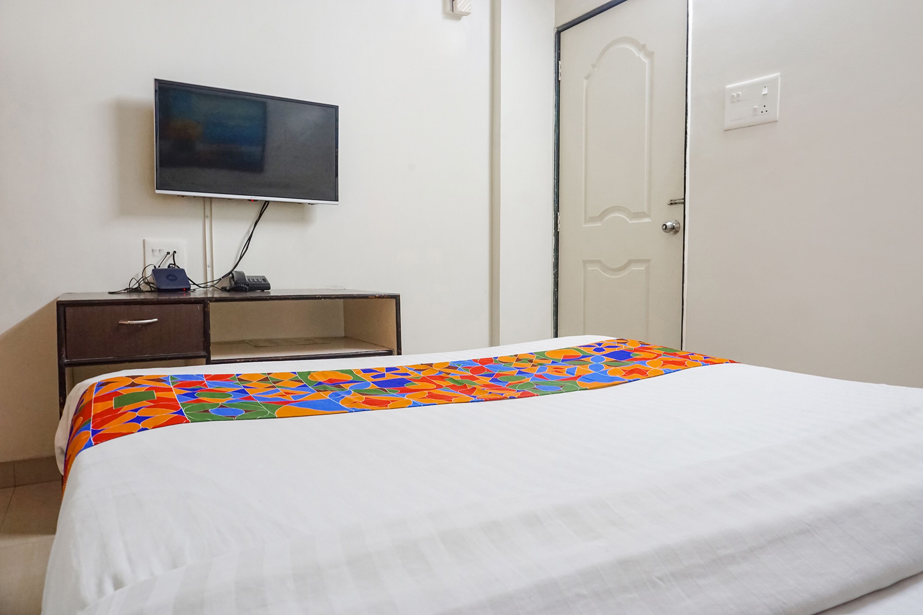 Une chambre d’hôtel avec un lit, un téléviseur fixé au mur, un bureau avec un ordinateur et une porte.
