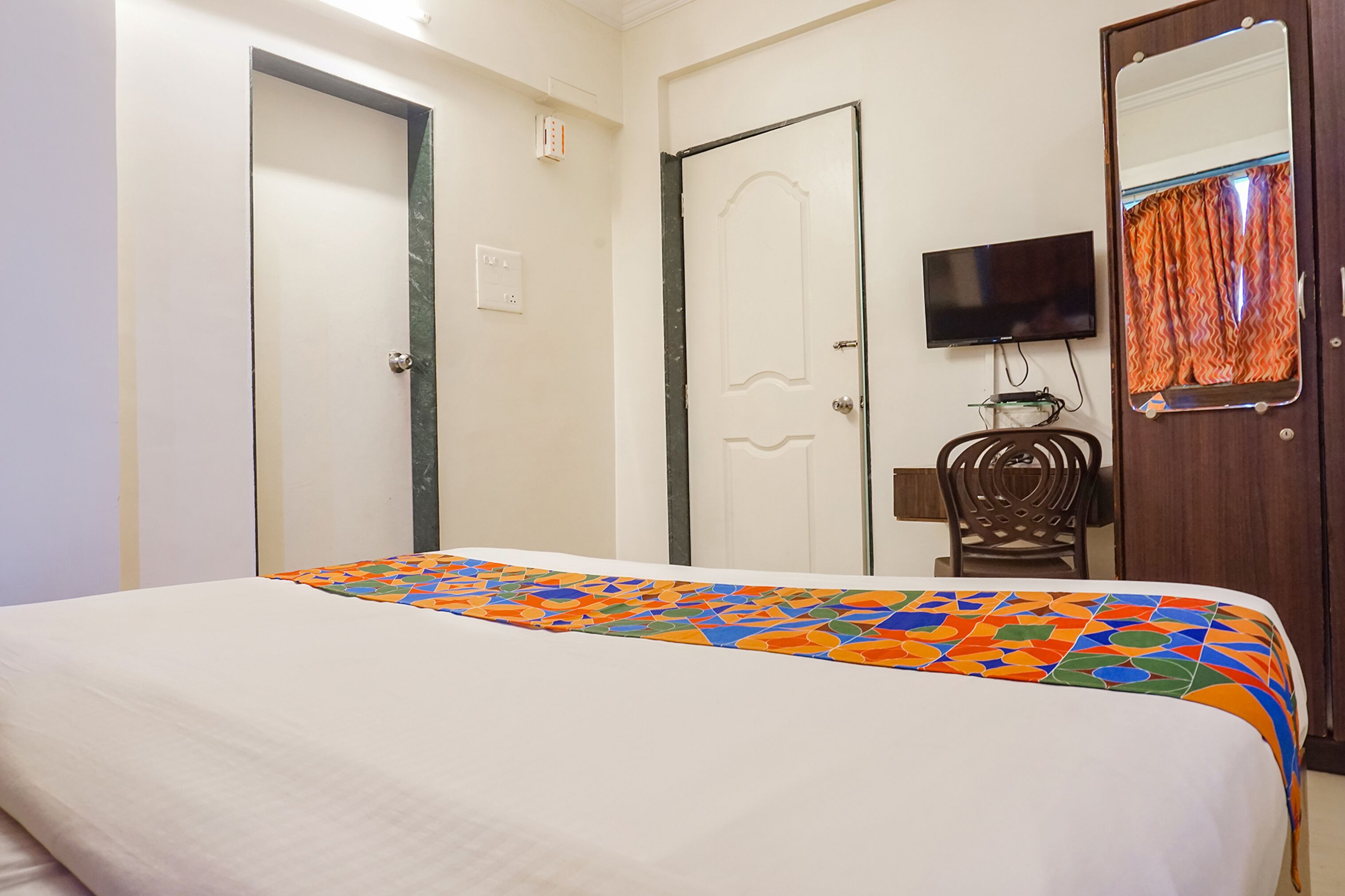Una habitación de hotel con una cama, televisión, silla y puerta.