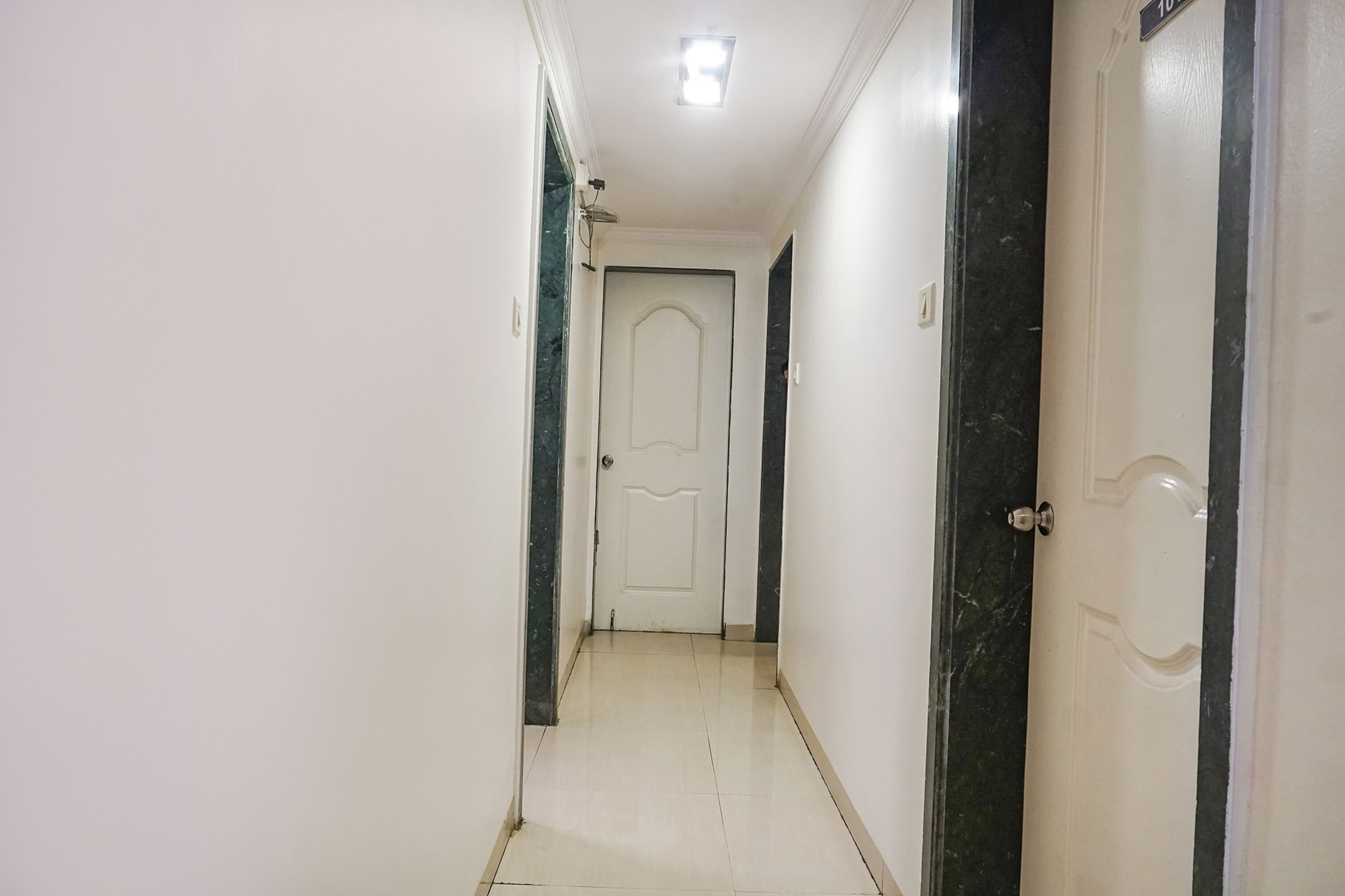 A narrow hallway with a white door at the end, a light fixture on the ceiling, and a black and white door on the right.