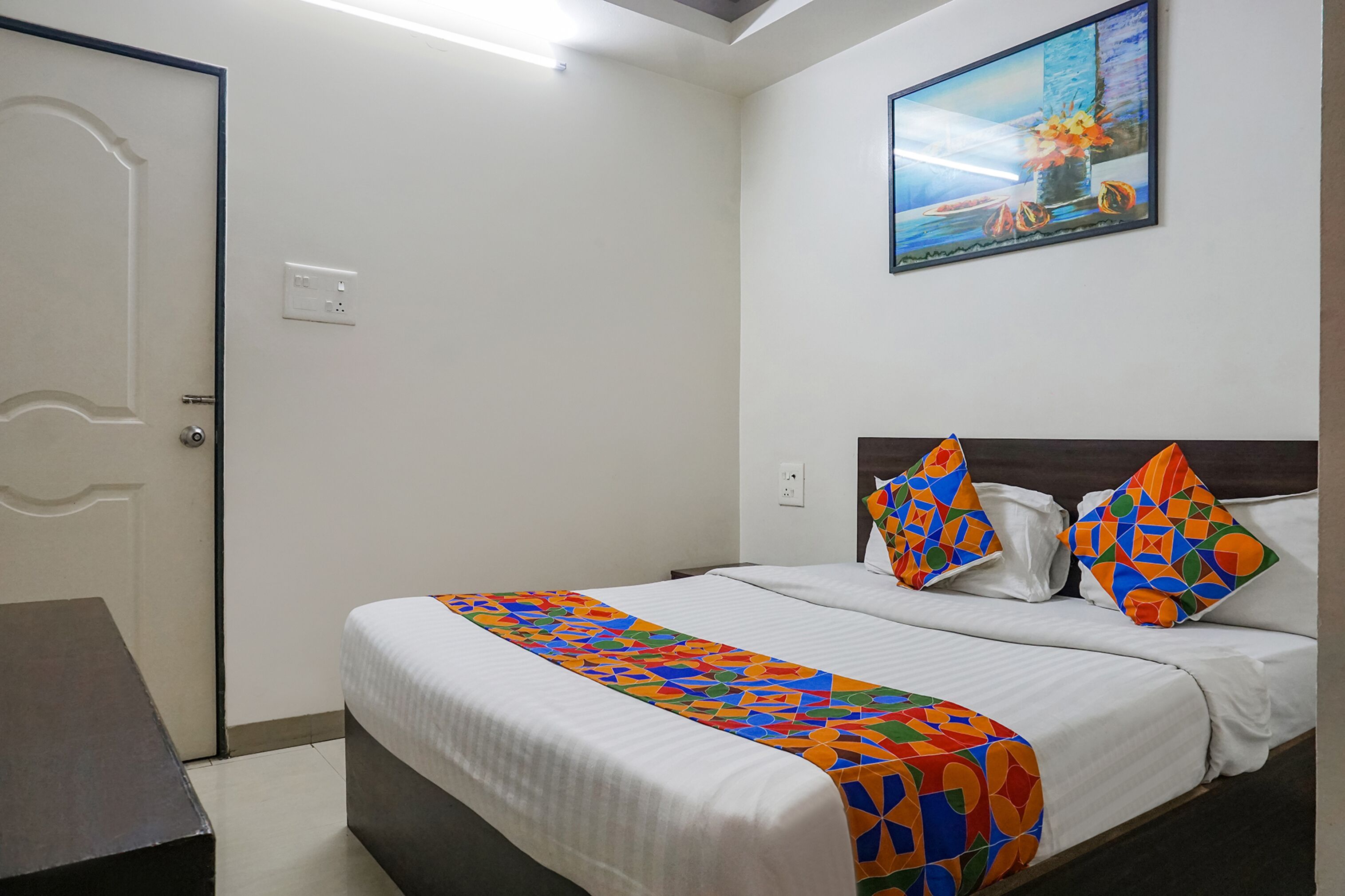 A hotel room with a bed, a desk, a painting on the wall, and a door.