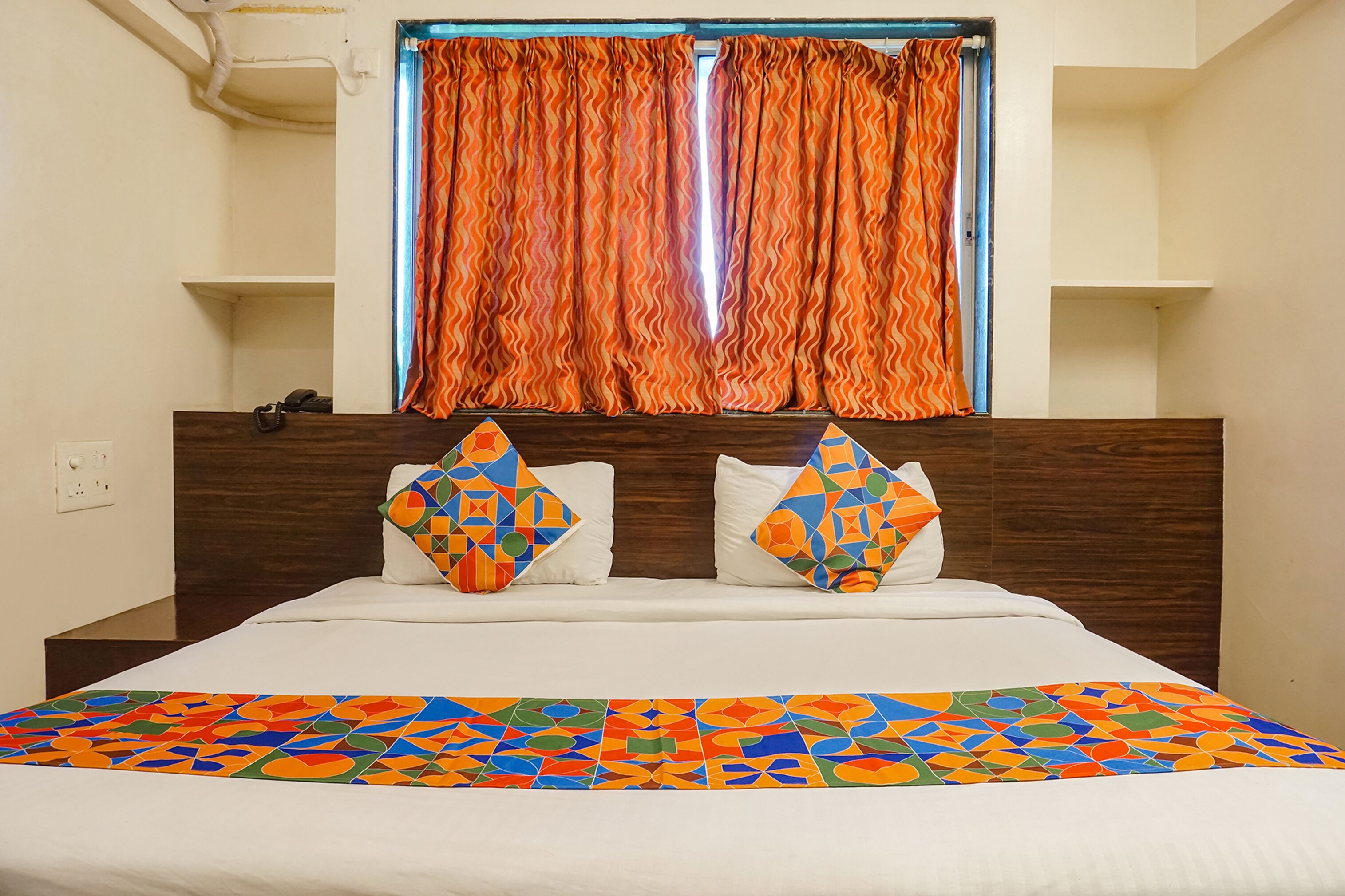 Un lit bien fait, agrémenté d’une couvre-lit aux motifs géométriques colorés, d’une tête de lit en bois et de deux coussins décoratifs.