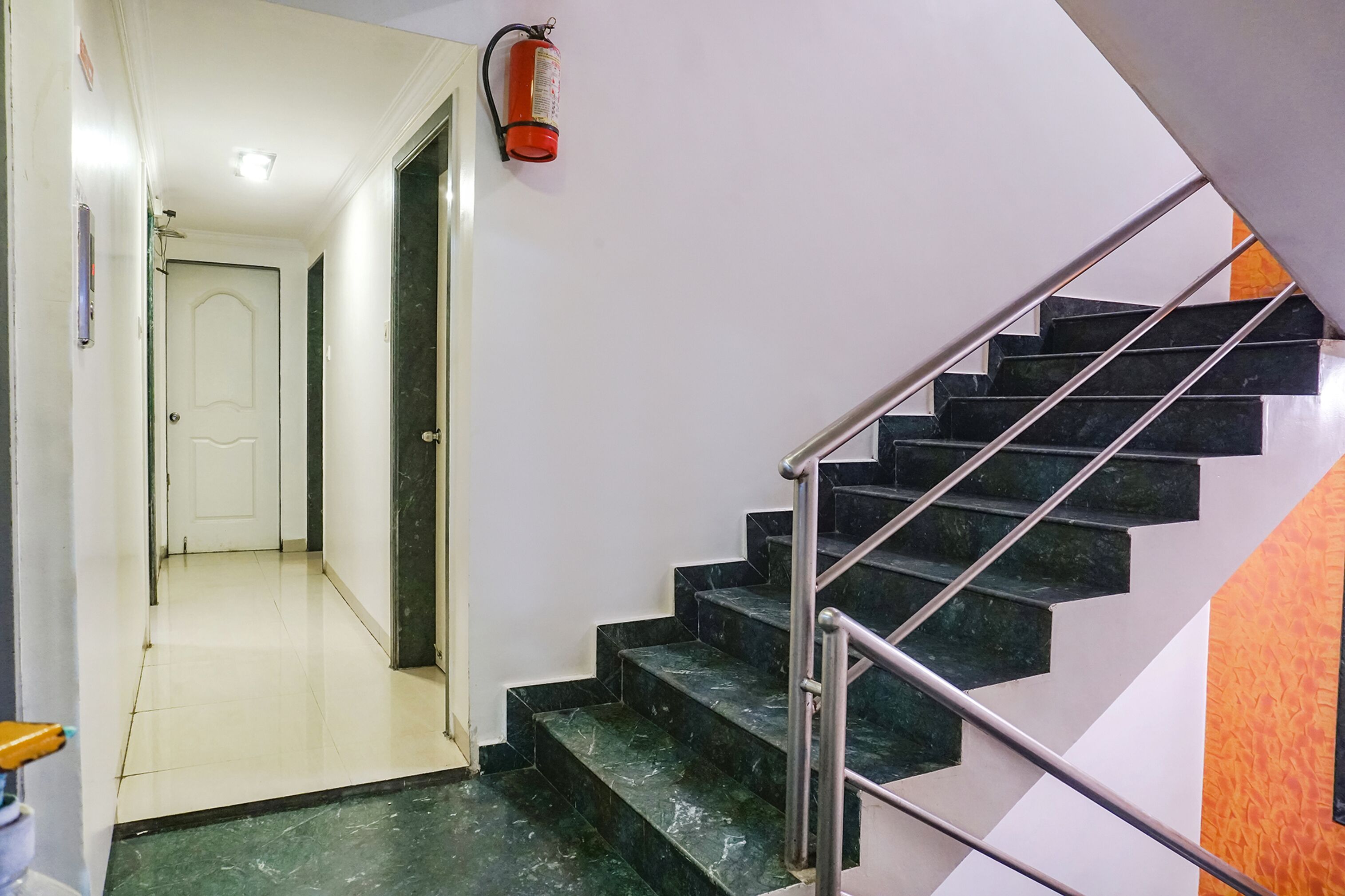 Una escalera con escalones de mármol negro y barandilla de metal que lleva a un rellano con una puerta blanca.