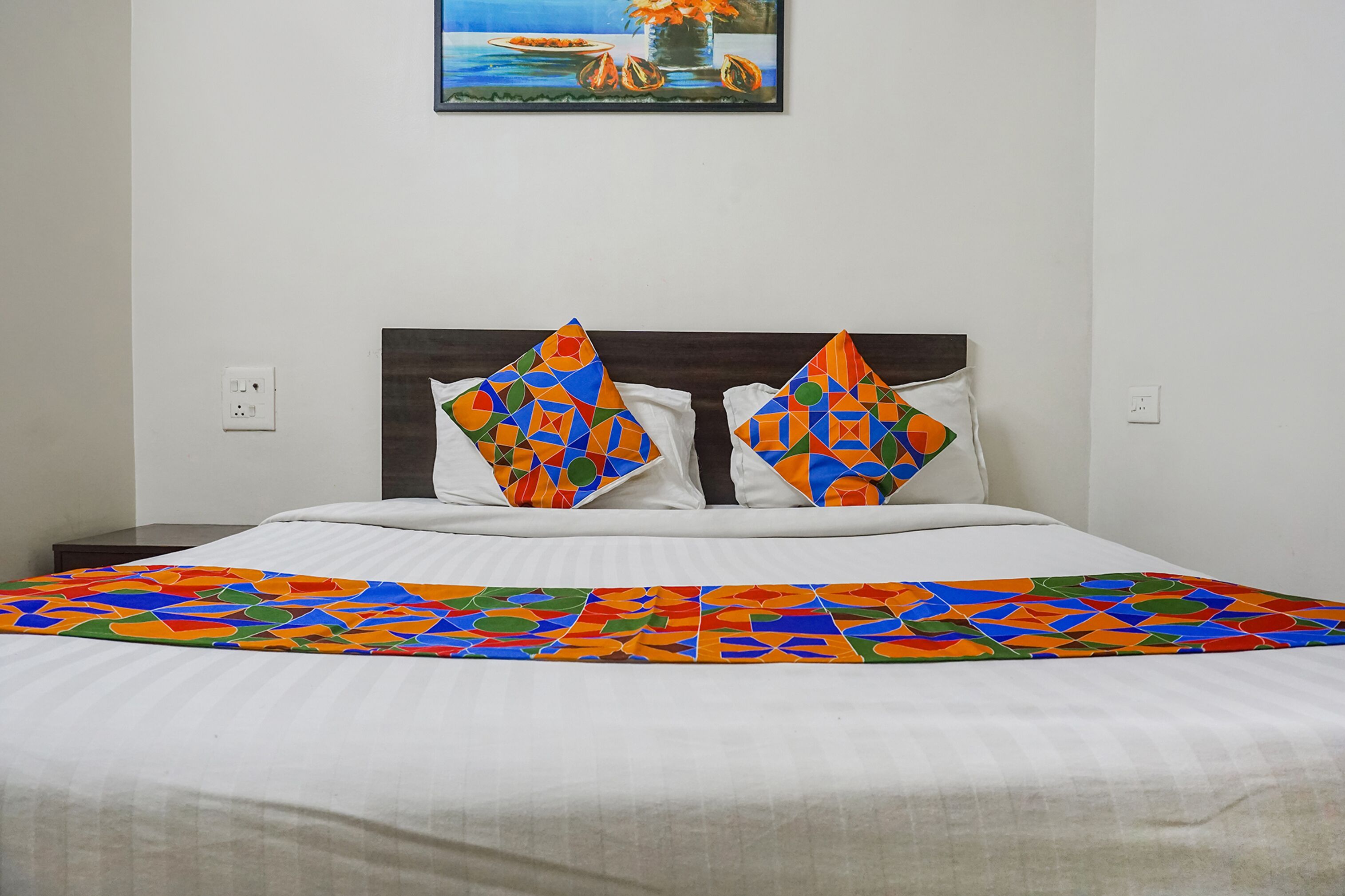 Cama com colcha de padrão geométrico colorido e duas almofadas com design semelhante.