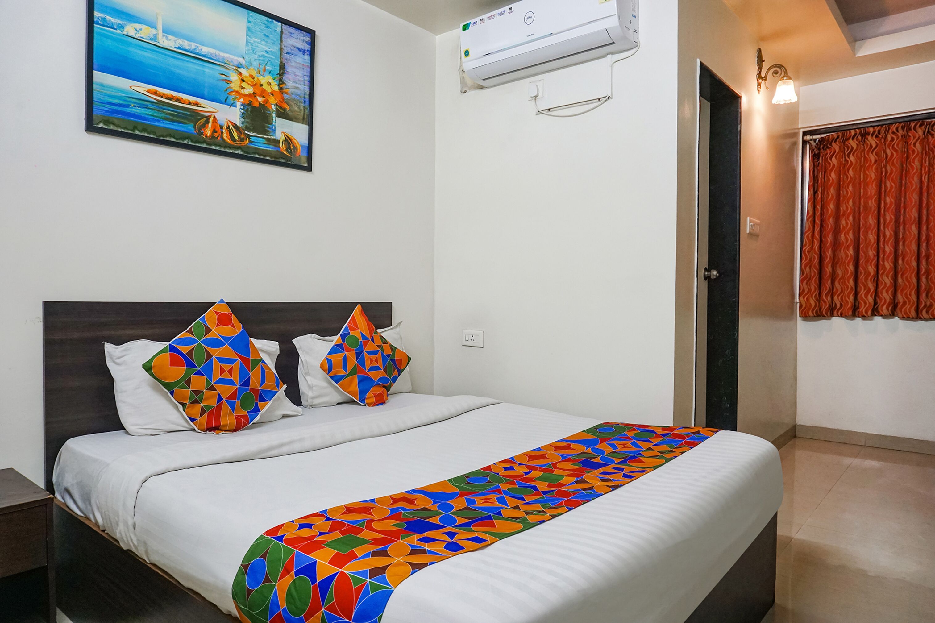 A neatly made bed with white linens, two colorful geometric pillows, and a multicolored blanket.