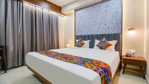 A hotel room with a large bed, a headboard with geometric patterns, a bedside table with a lamp, and a view of the city through the window. - Fabhotel Prime Ocean Breeze (Bhopal)