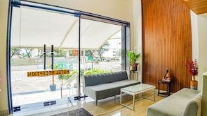 A modern interior with a sofa, a glass table, and a view through large glass doors. - Fabhotel Prime Ocean Breeze (Bhopal)