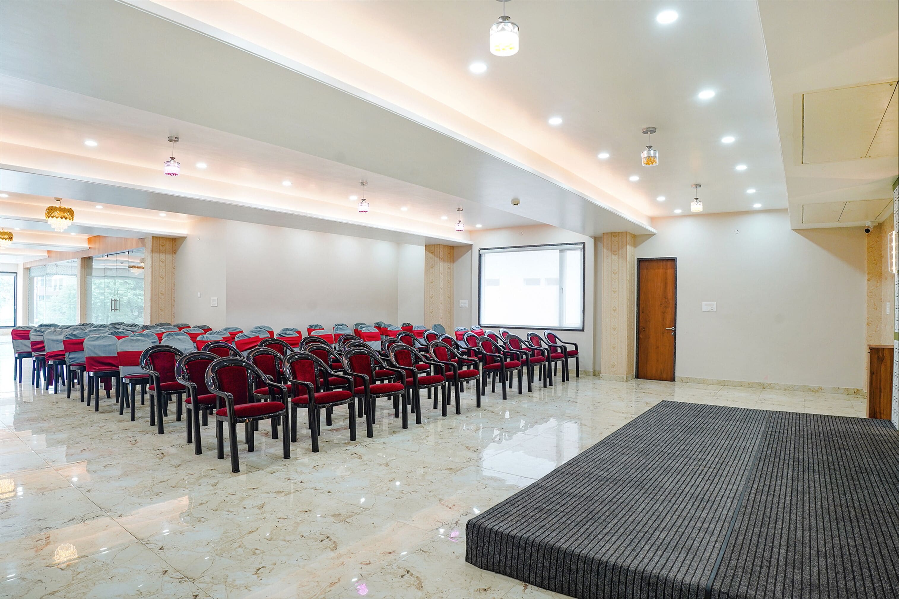 A conference room with rows of red chairs, a projector screen, and a large window.